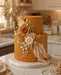 Decorative cake covered with Autumn Gold sugarpaste by Beau products, with flowers on a kitchen counter.