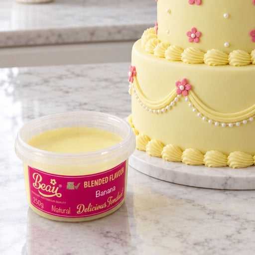 A container of Beau blended banana flavouring sits on a marble countertop next to a yellow decorated cake.