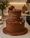 Two-tiered chocolate birthday cake made with Beau Products Chocolate Brown sugarpaste, with floral decorations on a kitchen counter.