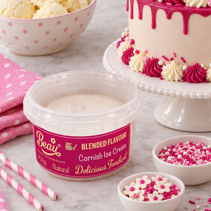 A tub of Beau's Blended Flavour Cornish Ice Cream placed on a marble surface, surrounded by pink and white dessert props including a decorated cake, bowls of sprinkles, ice cream, and striped straws.