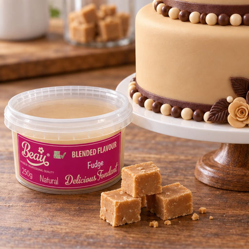A tub of Beau Blended Flavour Fudge on a wooden table, with several small brown fudge cubes in front and a decorated cake on a stand in the background.