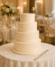 Five-tiered wedding cake covered with Ivory coloured sugarpaste by Beau products, on a table with a decorative tablecloth in a banquet hall setting.