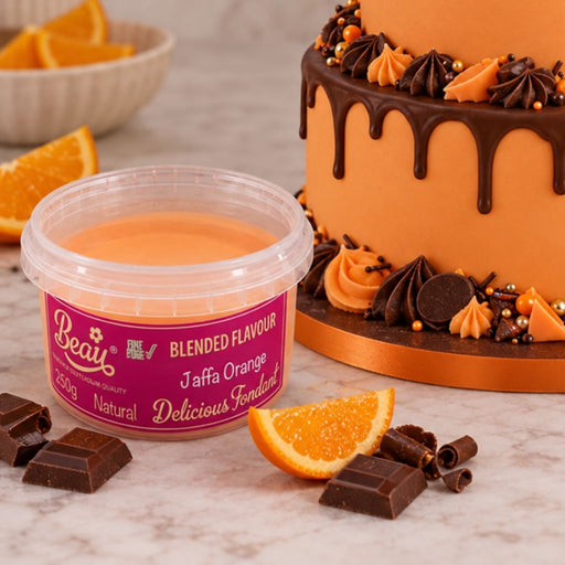 A tub of Beau's Jaffa Orange blended flavouring with confectionery sweets sits on a marble surface, styled with orange slices, chocolate pieces, and a decorated orange and chocolate cake in the background.