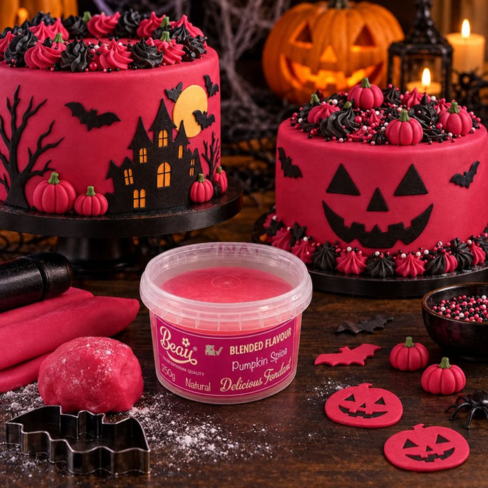 A tub of pink Halloween-themed frosting sits on a dark wooden table surrounded by decorated cakes, pumpkin cookies, black bat cutters, and festive props. The tub label reads Beau Blended Flavour Pumpkin Spice.