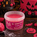 A tub of Beau Blénded Flavour Pumpkin Spice Fondant shown in a Halloween-themed setting with pink and black decorated cakes, fondant pieces, and small pumpkin decorations on a dark wooden surface.