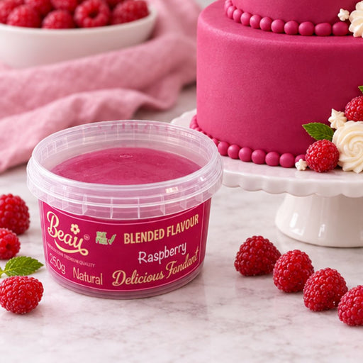 A tub of Beau Raspberry Delicious Fondant gelatin in the foreground, with fresh raspberries scattered around it and a pink frosted cake on a stand in the background.