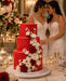Red wedding cake covered with Beau products Red Poinsettia sugarpaste with white flowers on a table with two brides in the background.