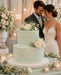 Wedding cake covered with Soft Sage coloured sugarpaste from Beau products, with floral decorations in front of a bridal couple.